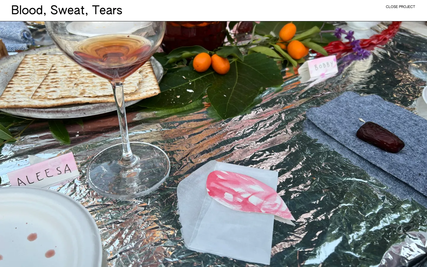 The desktop page features a large hero image of a Passover Seder table set with matzah, wine, citrus, and a pink tear-shaped paper note on a reflective foil tablecloth. The headline 'Blood, Sweat, Tears' is positioned at the top left, with a 'CLOSE PROJECT' link at the top right. The layout is clean with a minimalist white background for text elements.