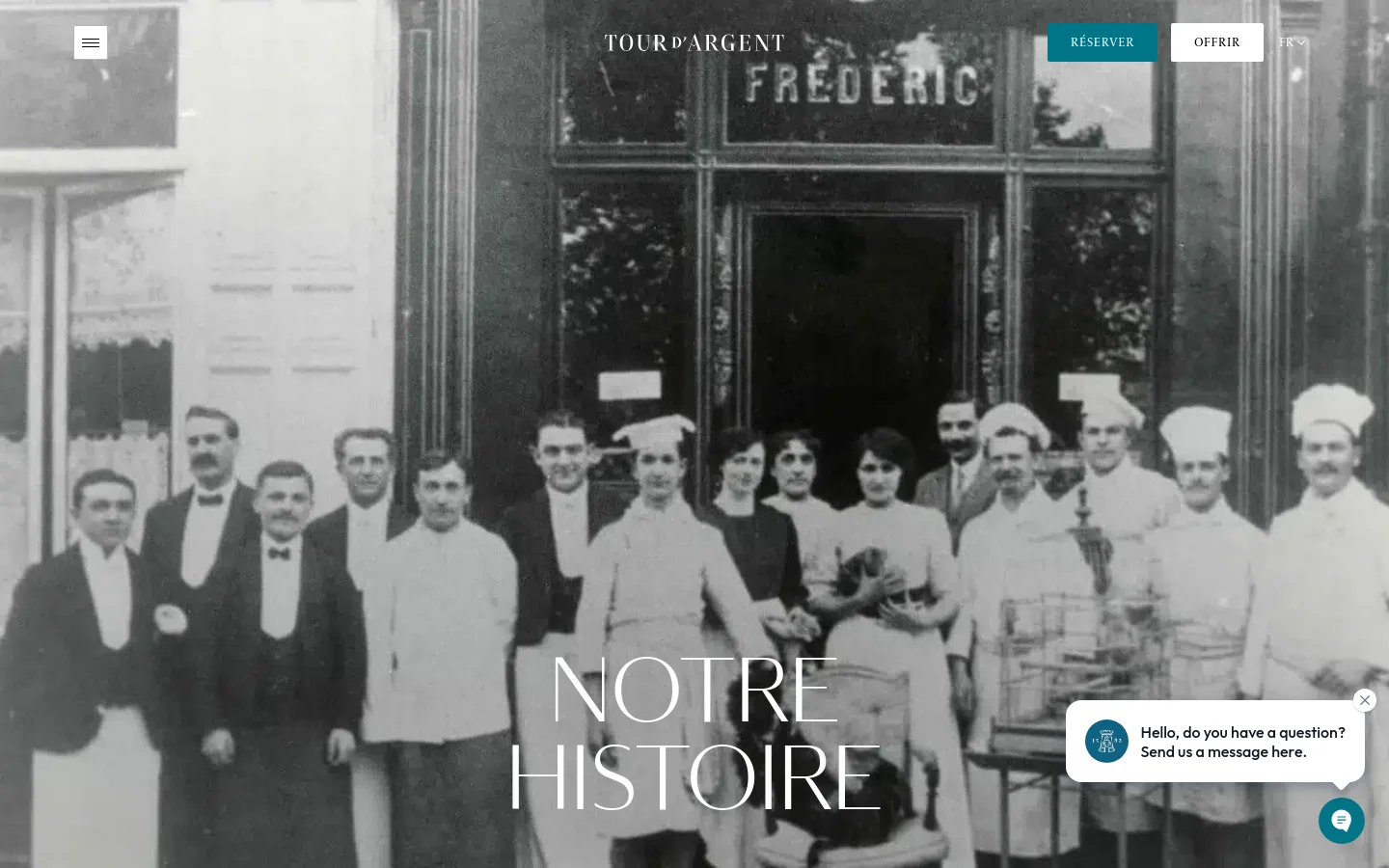 The desktop page features a large, black-and-white hero image of a historical group of restaurant staff in formal attire, overlaid with the large white title 'NOTRE HISTOIRE'. A navigation bar at the top includes the 'TOUR D'ARGENT' logo, a 'RÉSERVER' button in teal, and an 'OFFRIR' button. A small chat widget is visible in the bottom right corner.