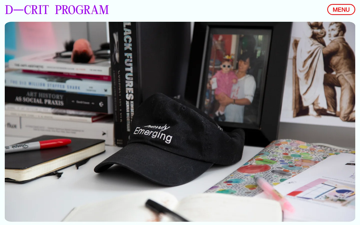The desktop page features a large hero image of a desk with books, a black baseball cap, and notebooks, with the purple headline 'D-CRIT PROGRAM' at the top left and a 'MENU' button at the top right. Below the image, purple and black text describes the MA in Design Research, Writing & Criticism program against a clean white background.