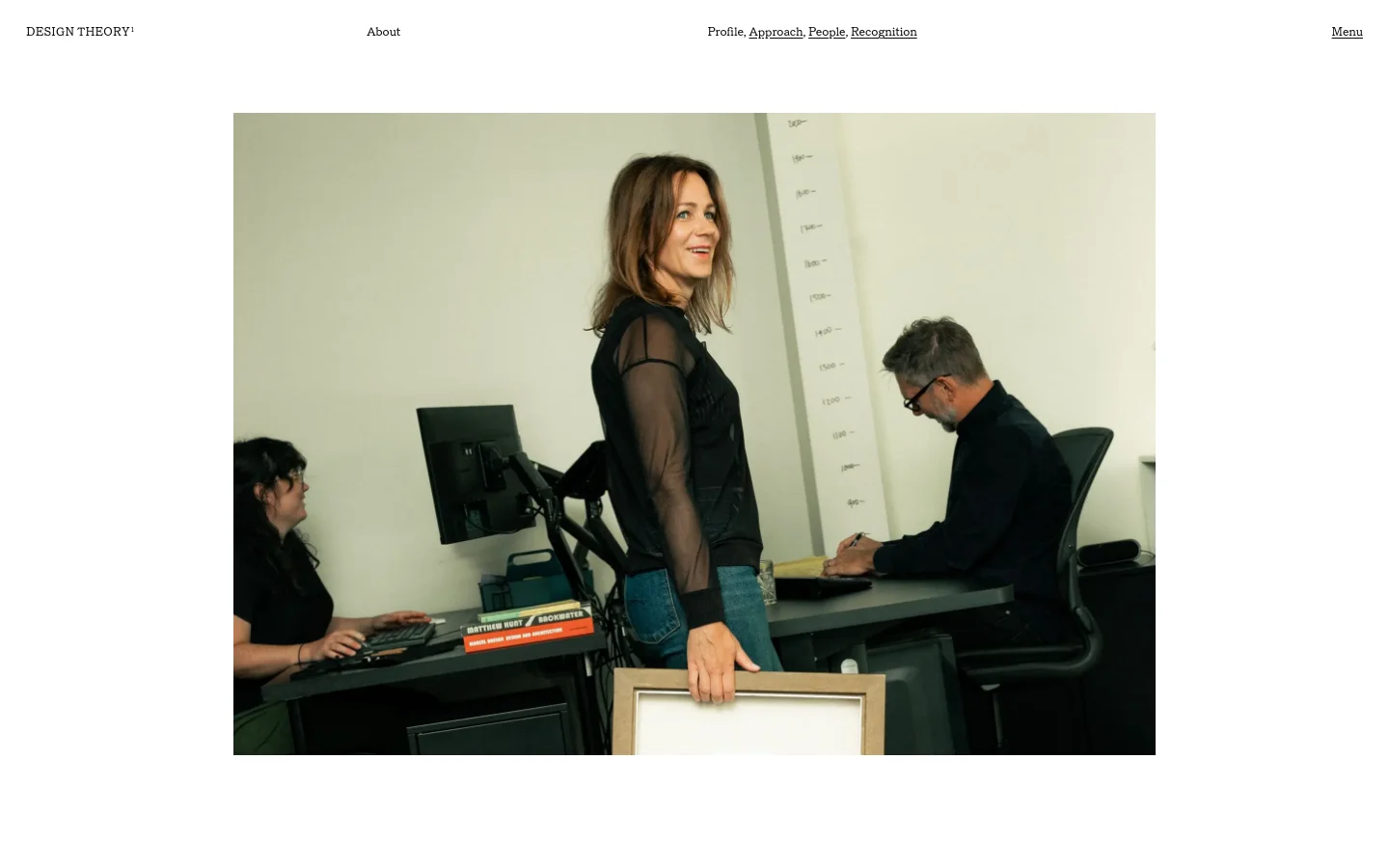 Design Theory about page featuring a minimalist editorial layout with large-scale photography. The hero section displays a candid studio photograph of designers at work, set against a clean white background with sophisticated serif typography and a simple navigation menu.