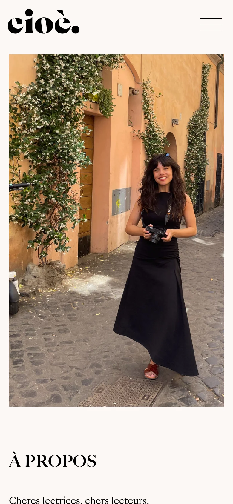 The mobile version displays a large hero image of a smiling woman in a black dress holding a camera, standing in a sunlit cobblestone alleyway with climbing plants. Above the image, the black 'cioè.' logo is left-aligned next to a hamburger menu icon. The 'À PROPOS' headline and text follow below the image in a single-column vertical stack.