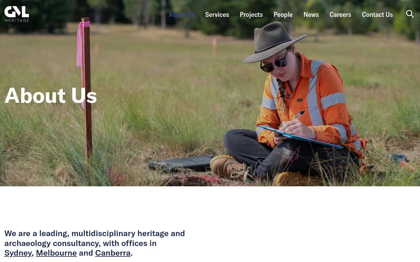 The desktop page features a large hero image of an archaeologist in high-visibility clothing sitting in a field, overlaid with the white headline 'About Us'. A navigation menu is at the top right, and the main content area below uses dark text on a white background to describe the company's multidisciplinary services.
