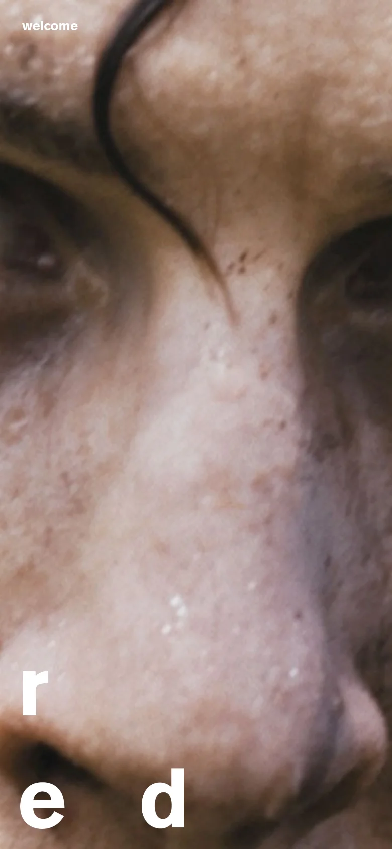 The mobile version maintains the cinematic close-up video background but scales the content for a vertical aspect ratio. The large white 'red' text is positioned at the bottom left, and the 'welcome' link remains at the top left.