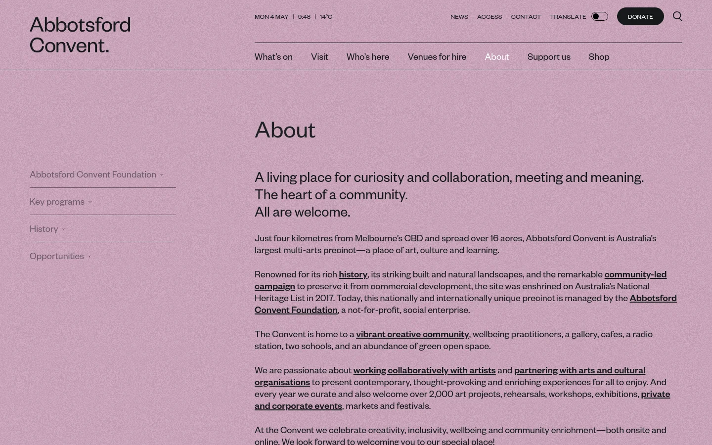 The desktop About page features a minimalist design with a soft pink textured background and dark navy text. A large 'About' heading sits above a vertical navigation menu containing links for Abbotsford Convent Foundation, Key programs, History, and Opportunities. The main content area includes a large headline about curiosity and community, followed by descriptive text about the precinct's history and mission.
