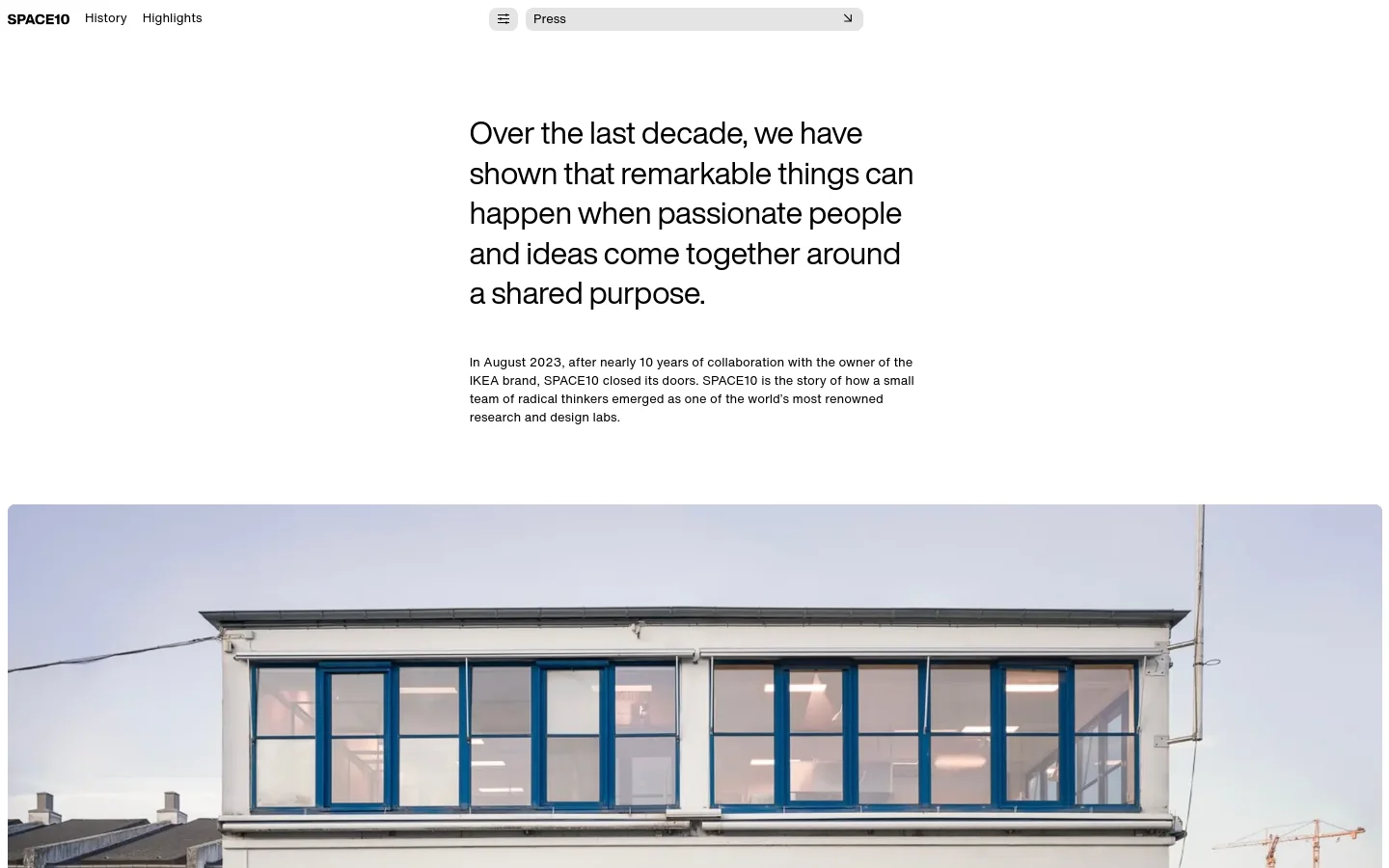 The desktop page features a minimalist white layout with large, black serif typography for the main headline. Below the introductory text is a wide, cinematic photograph of a modern white building with large blue-framed windows under a pale sky. The navigation menu is positioned at the top right with links for History and Highlights.
