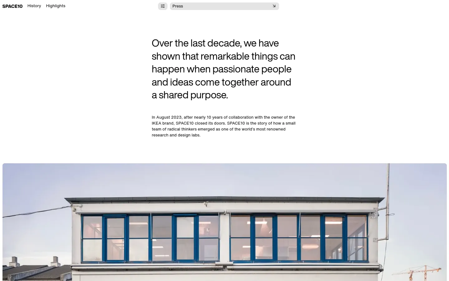 The desktop page features a minimalist white layout with large, black serif typography for the main headline. Below the introductory text is a wide, cinematic photograph of a modern white building with large blue-framed windows under a pale sky. The navigation menu is positioned at the top right with links for History and Highlights.