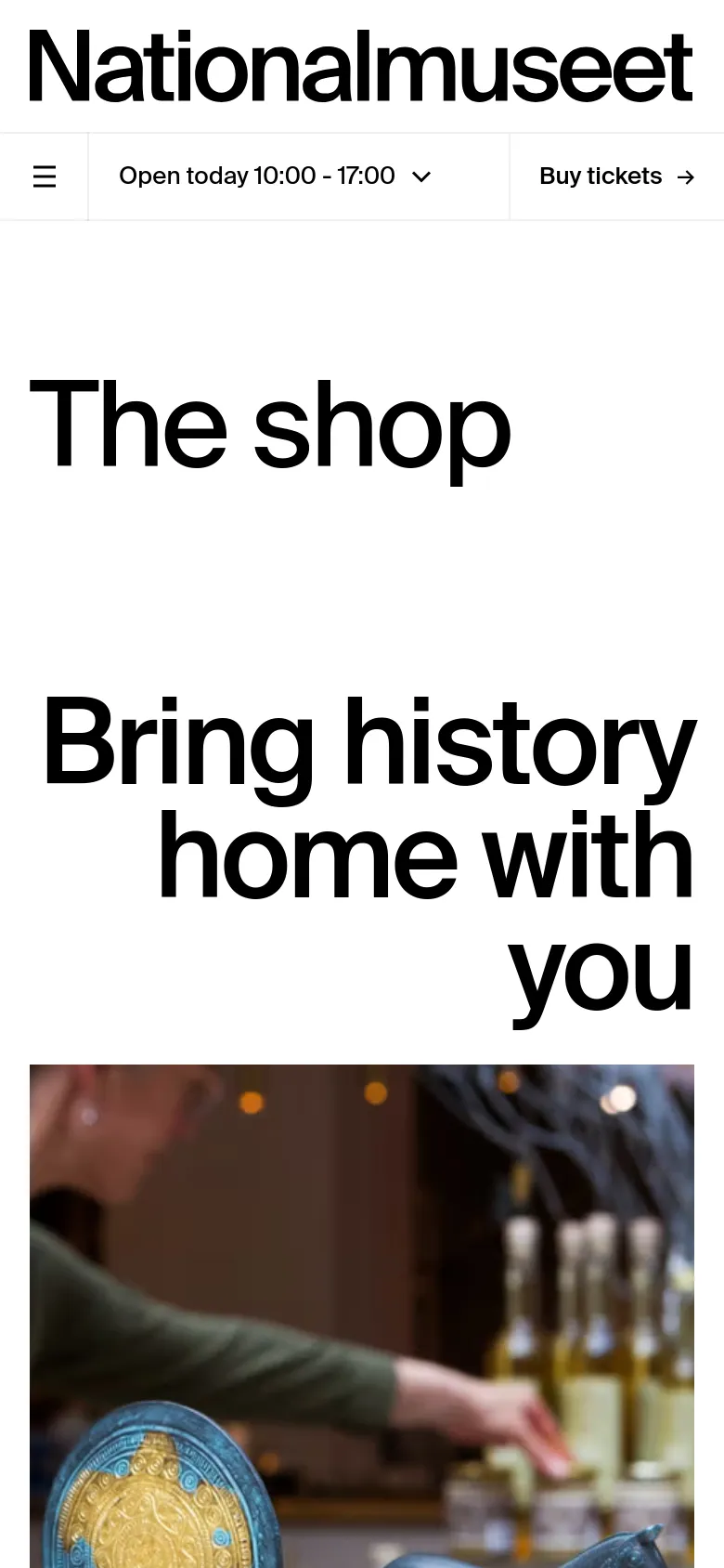 The mobile version presents a vertically stacked layout optimized for small screens, with the large 'The shop' headline and 'Bring history home with you' subheadline appearing above a hero image. The navigation is condensed into a hamburger menu, and a prominent 'Buy tickets' call-to-action button is visible in a sticky header alongside the museum's opening hours.