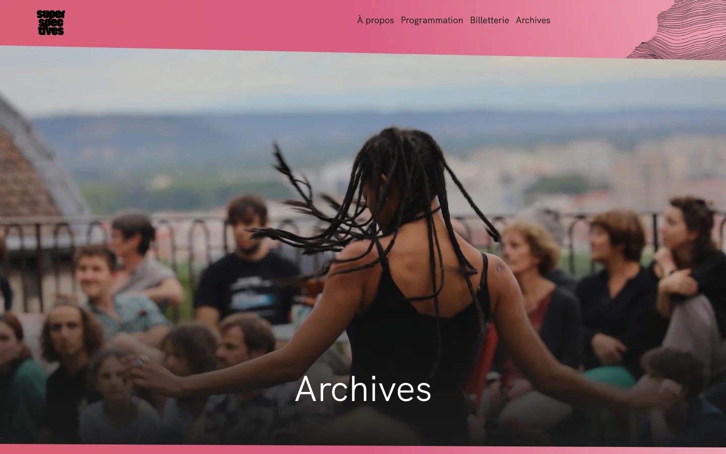 The Archives page features a large hero image of a person with long braids performing outdoors, overlaid with the white title 'Archives'. A pink header contains the Superspectives logo on the left and a navigation menu on the right. The layout is clean with a minimalist aesthetic and a dominant pink and dark photographic color palette.
