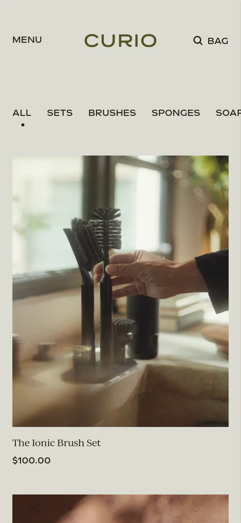 The mobile version of the Curio homepage uses a simplified layout with a condensed header containing a hamburger menu, the brand logo, and a search icon. The product category navigation is displayed in a single horizontal row, and the product imagery is stacked vertically in a single-column view to optimize for smaller screens.