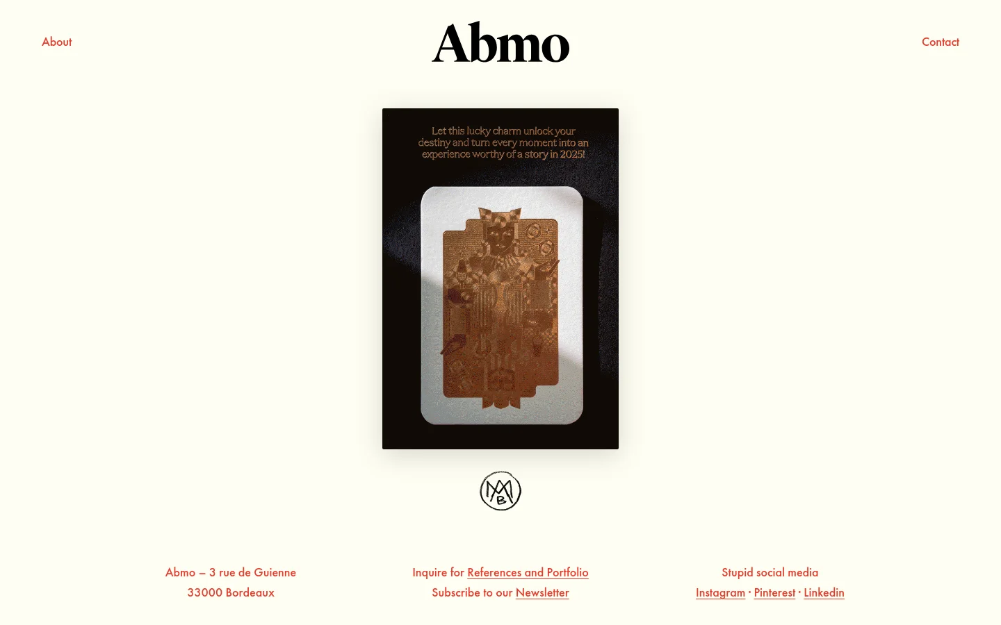 The Abmo homepage features a minimalist design with a cream background and black serif typography. The layout includes a centered 'Abmo' logo, navigation links for 'About' and 'Contact' on either side, and a large central hero image of a textured, embossed card design. The footer contains contact information, portfolio links, and social media links in red text.
