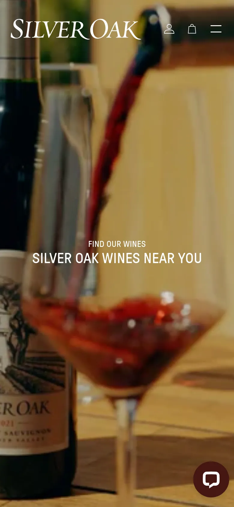 The mobile version uses the same wine-pouring hero image but crops it vertically to fit the screen, with the navigation condensed into a hamburger menu and user icons at the top. The headline 'SILVER OAK WINES NEAR YOU' remains centered, and a circular chat icon is anchored to the bottom right corner.