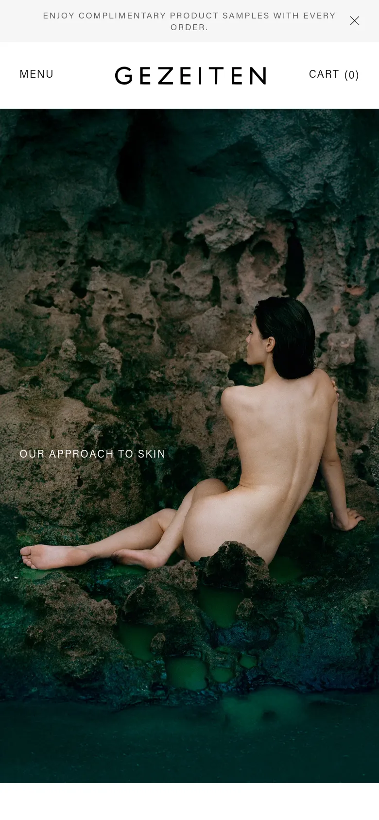 The mobile version simplifies the header, replacing the full navigation bar with a 'MENU' text link on the left and 'CART (0)' on the right, flanking the centered GEZEITEN logo. The hero image of the woman on the rocky coast is scaled to fit the vertical screen, maintaining the same dark, natural aesthetic and 'OUR APPROACH TO SKIN' text overlay.