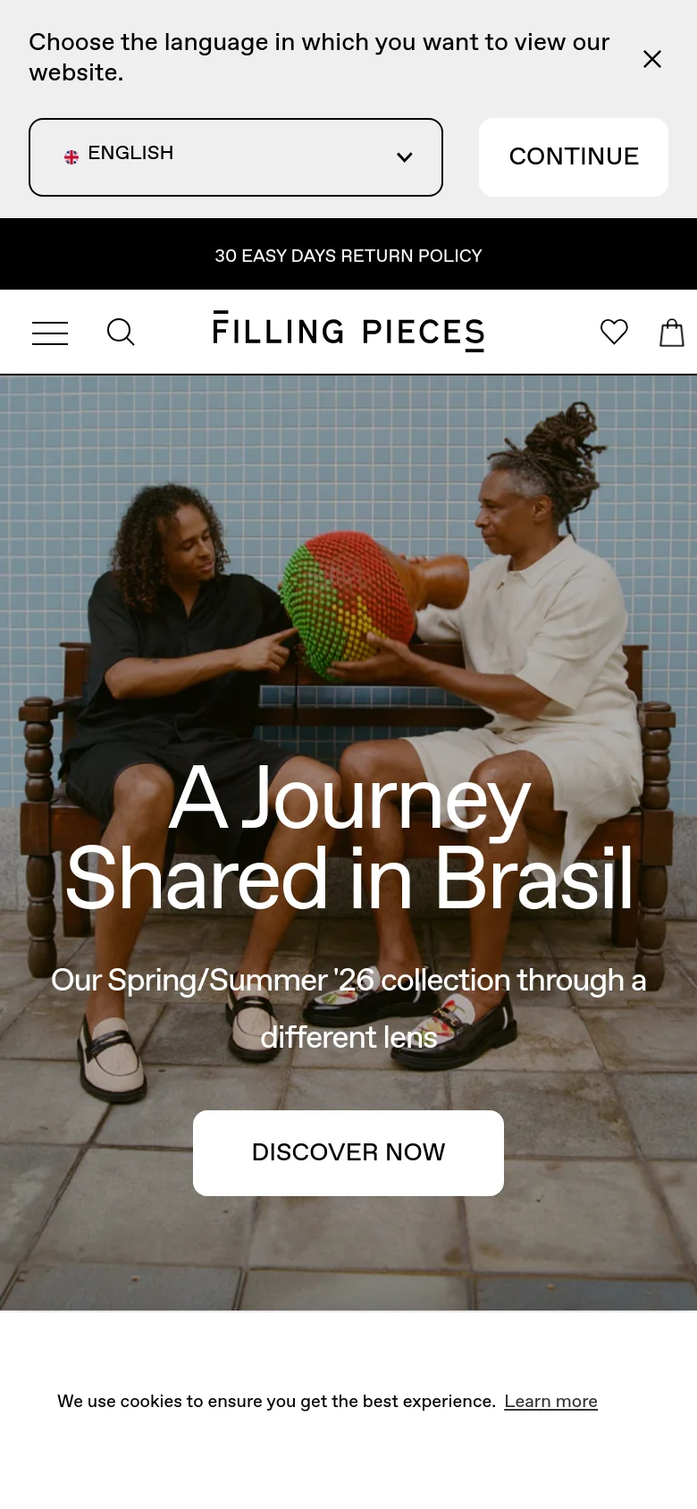 The mobile version presents a vertically stacked layout centered around the hero image of two people on a bench. The headline 'A Journey Shared in Brasil' and the 'DISCOVER NOW' call to action are prominently centered, while the navigation is condensed into a hamburger menu and search icon. A large language selection prompt and cookie notice occupy the top and bottom of the screen.