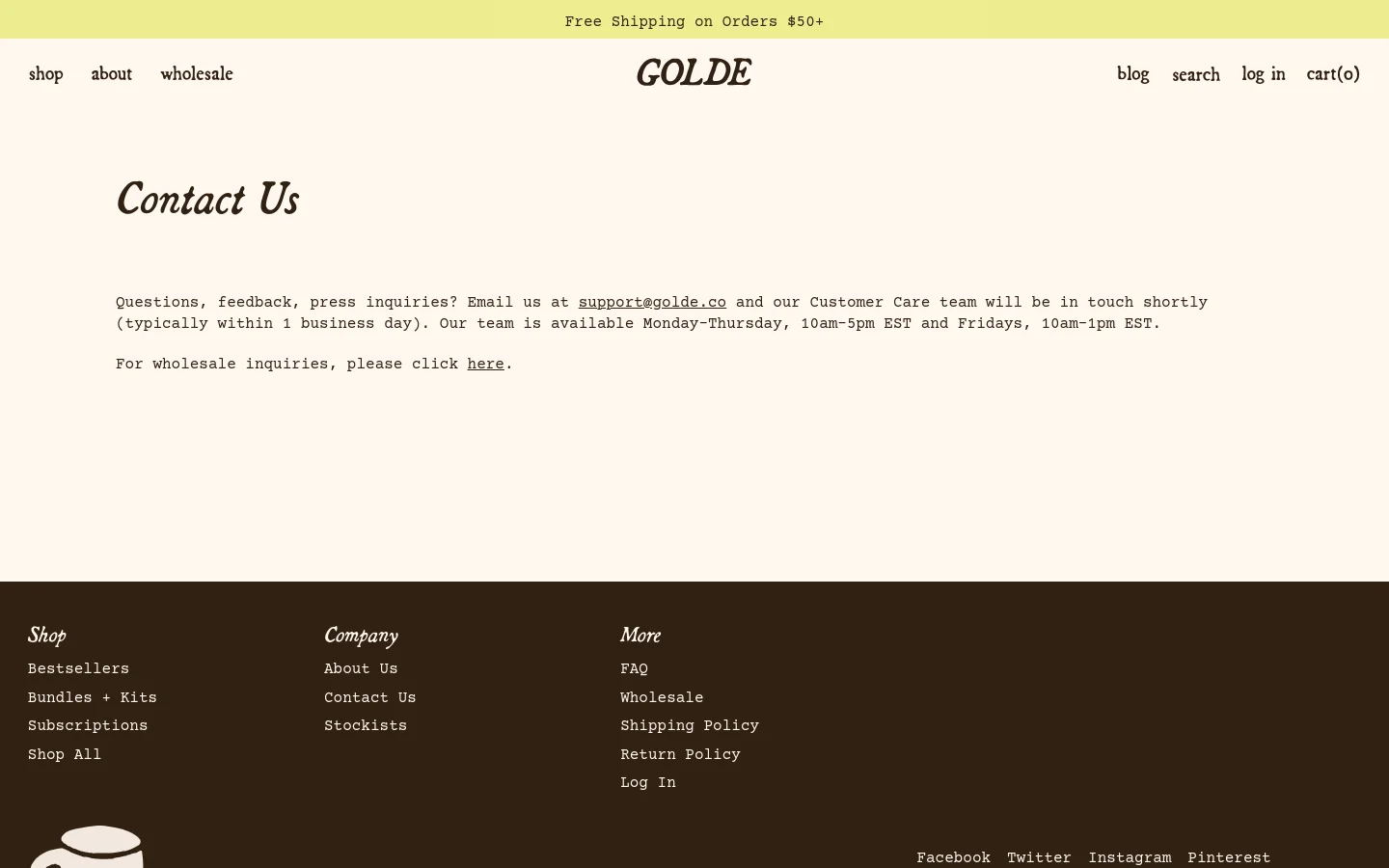 The desktop Contact Us page features a minimalist design with a cream background and dark brown text. The layout includes a top announcement bar for free shipping, a centered logo, and navigation links for shop, about, wholesale, blog, search, log in, and cart. The main content consists of a large 'Contact Us' headline followed by contact information and a wholesale inquiry link, with a dark brown footer containing site links.