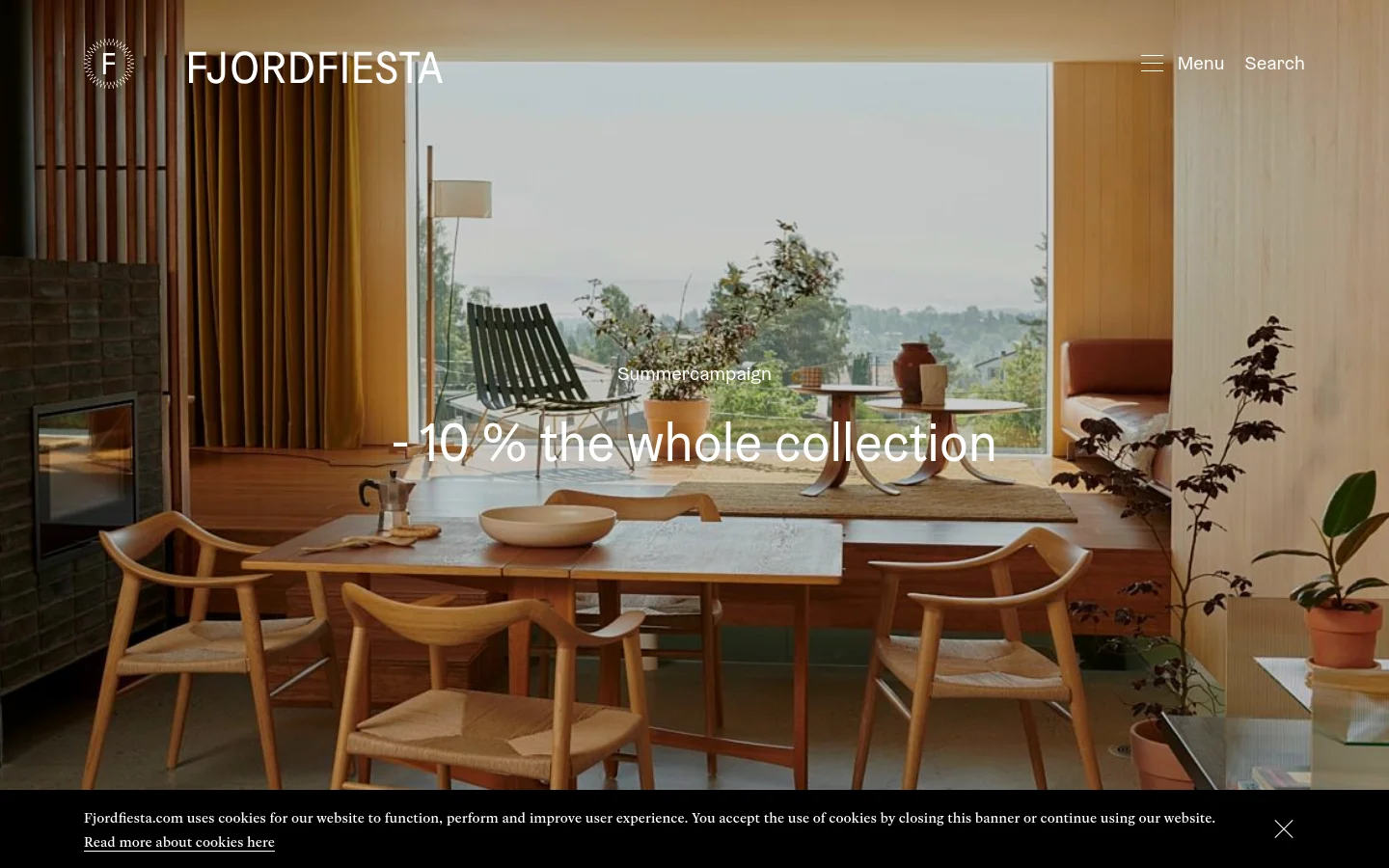The desktop homepage features a large hero image of a modern Scandinavian dining room with wooden furniture overlooking a misty landscape. The headline 'Summercampaign - 10% the whole collection' is centered over the image, with a navigation menu and search option in the top right. A black cookie consent banner spans the bottom of the screen.