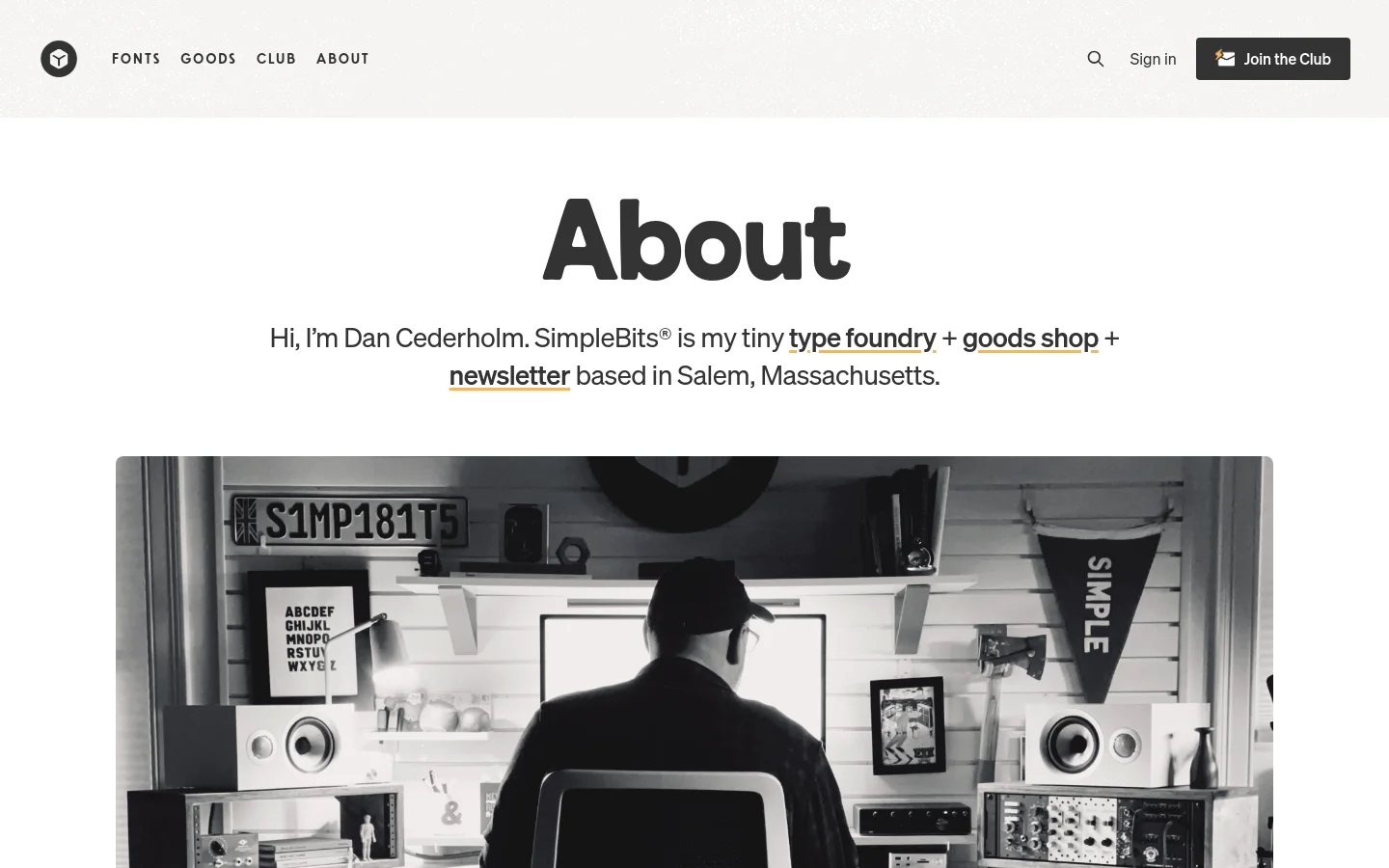 The About page features a large 'About' heading above a black and white hero image of a man working at a desk in a studio. A navigation bar at the top includes links for Fonts, Goods, Club, and About, alongside a 'Join the Club' button. The layout is clean with a white background and dark text.