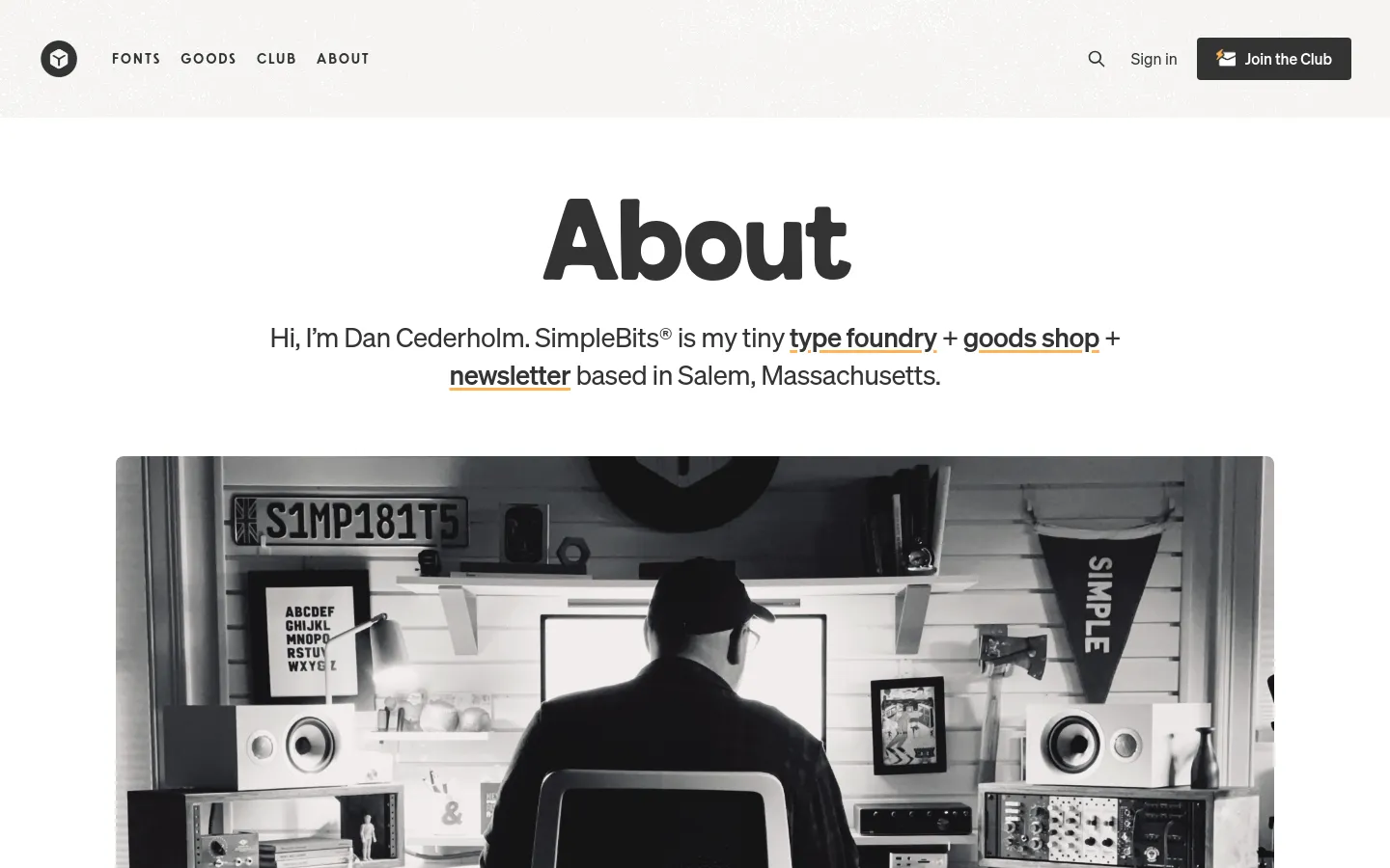 The About page features a large 'About' heading above a black and white hero image of a man working at a desk in a studio. A navigation bar at the top includes links for Fonts, Goods, Club, and About, alongside a 'Join the Club' button. The layout is clean with a white background and dark text.