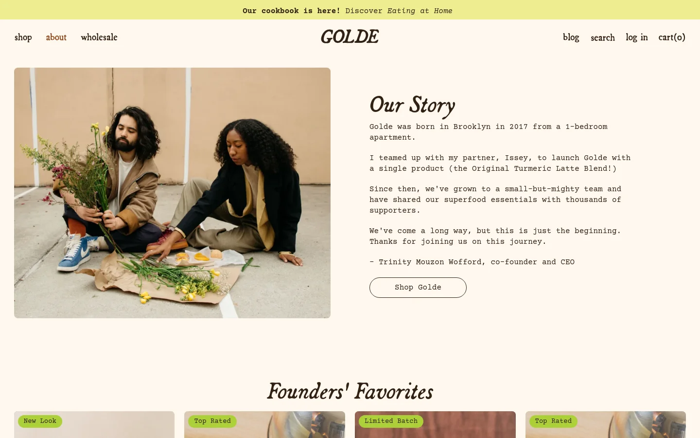 The desktop page features a large hero image on the left showing two founders sitting on the ground with flowers, next to an 'Our Story' text section on a cream background. Below this, a 'Founders' Favorites' section displays a grid of product cards with images, titles, and prices. The navigation bar is clean with links for shop, about, wholesale, blog, search, log in, and cart.