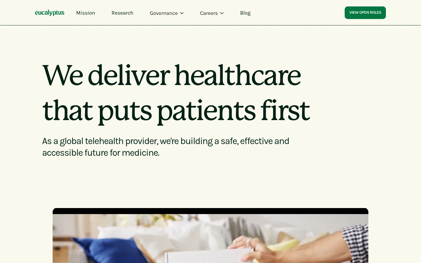 The desktop homepage features a clean, minimalist design with a cream background and dark green text. A large headline reads 'We deliver healthcare that puts patients first' above a subheadline, positioned next to a navigation menu containing links for Mission, Research, Governance, Careers, and Blog, with a prominent 'VIEW OPEN ROLES' button. Below the hero section, a large lifestyle image shows a person in a domestic setting, partially obscured by a chat interface overlay.