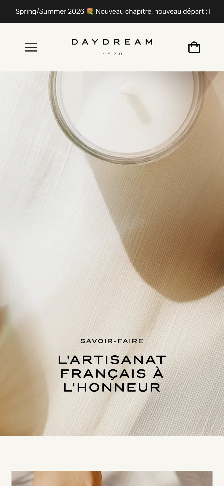 The mobile version presents a vertically oriented view of the hero image, focusing on the close-up of a candle and textured fabric. The headline 'SAVOIR-FAIRE L'ARTISANAT FRANÇAIS À L'HONNEUR' is centered in the lower half of the screen. The header is simplified with a hamburger menu icon on the left, the brand logo in the center, and a shopping bag icon on the right.
