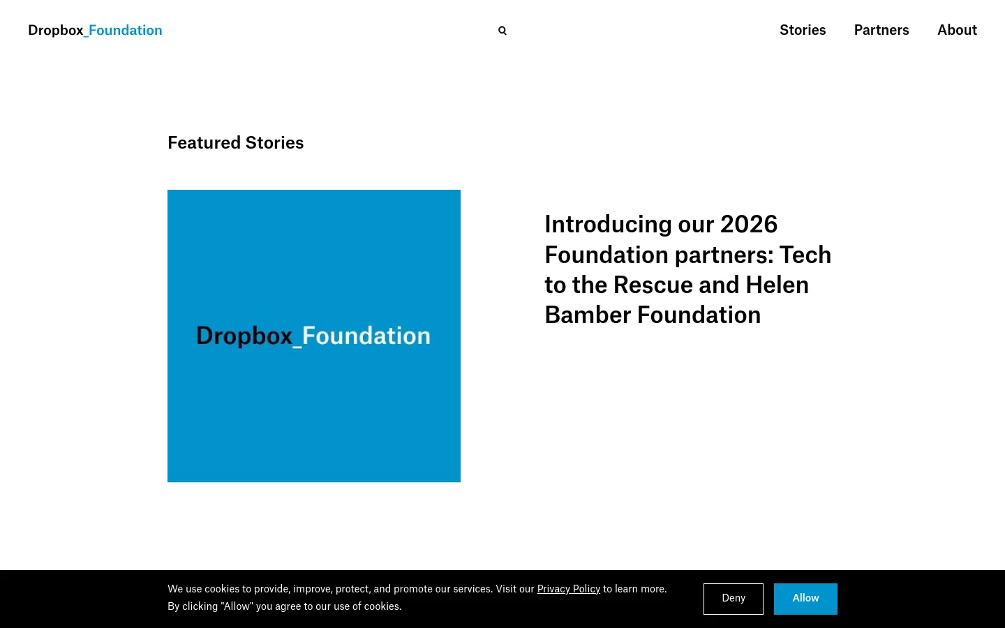 The desktop homepage for Dropbox Foundation features a clean, white layout with a navigation menu containing Stories, Partners, and About. A large hero section displays the headline 'Introducing our 2026 Foundation partners: Tech to the Rescue and Helen Bamber Foundation' next to a bright blue square containing the Dropbox Foundation logo. A cookie consent banner appears at the bottom of the screen.