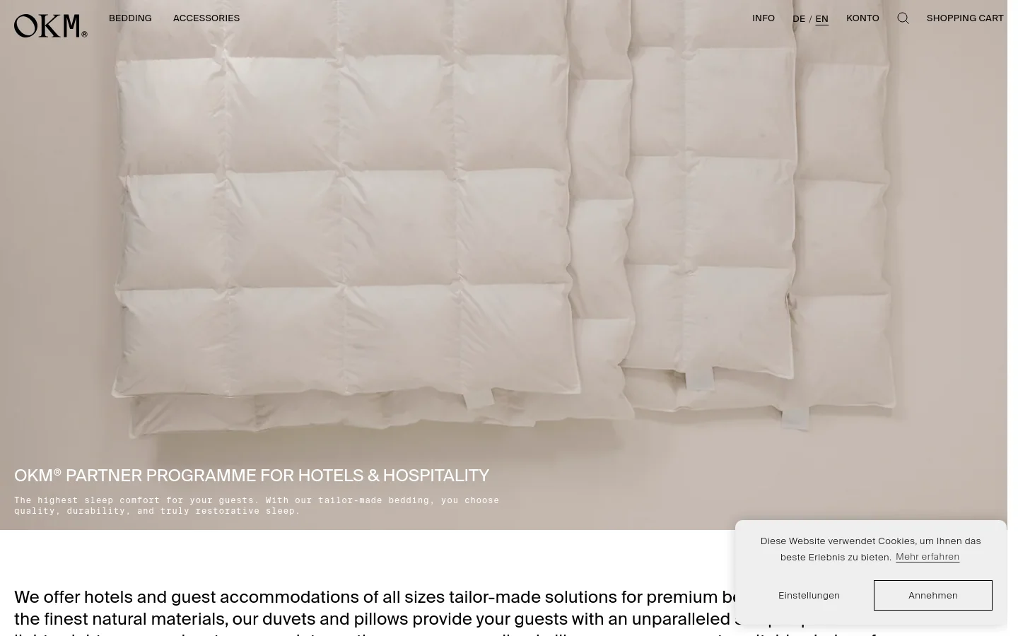 The desktop page features a large hero image of white, quilted duvets against a neutral background, with the headline 'OKM® PARTNER PROGRAMME FOR HOTELS & HOSPITALITY' overlaid in white text. A clean navigation bar at the top includes the OKM logo, categories like Bedding and Accessories, and links for Info, Language, Account, and Shopping Cart. Below the hero section, a white content area begins with text describing tailor-made bedding solutions for hotels.