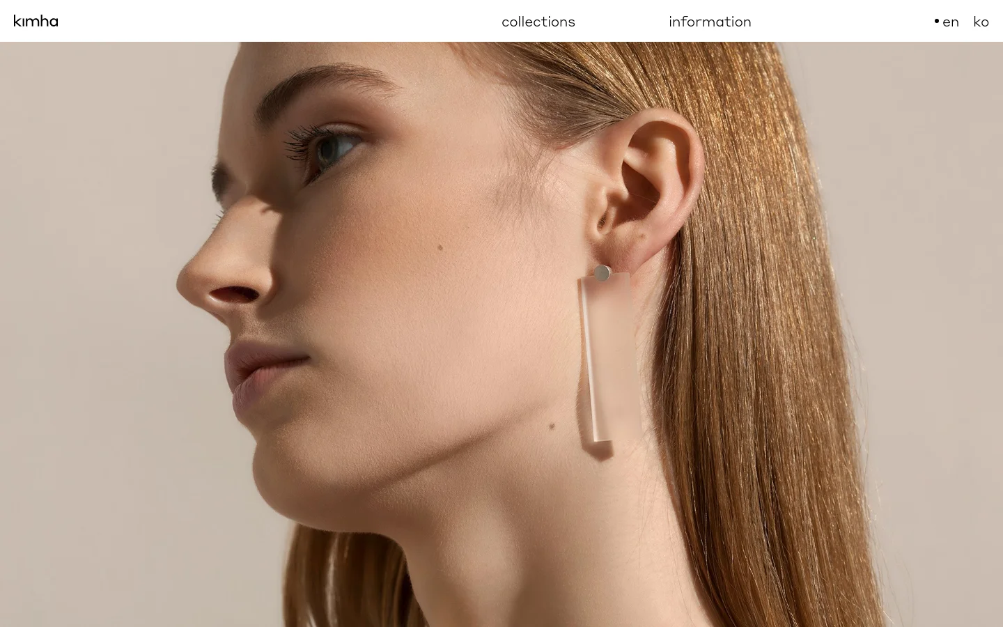 The desktop homepage features a minimalist design with a large, high-resolution hero image of a woman's profile wearing a frosted rectangular earring. The navigation bar at the top includes the brand name 'kimha' on the left, 'collections' and 'information' in the center, and language selectors on the right. A centered text link reads 'View the Collections' over the image.