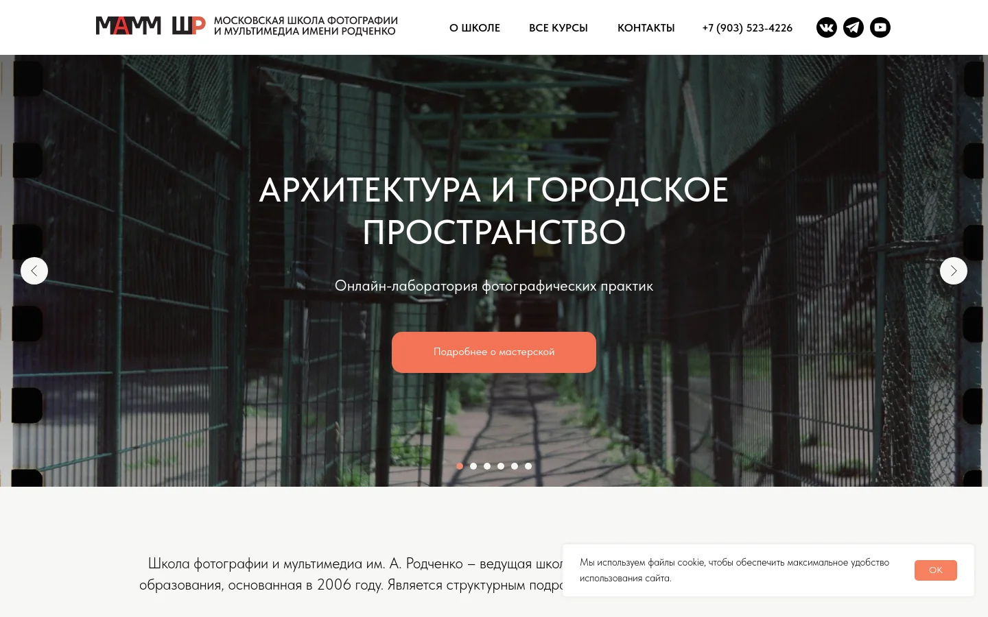 Desktop homepage for the Rodchenko School of Photography and Multimedia featuring a large hero image slider showing a fenced urban walkway. The navigation bar includes the school logo, links for 'About', 'All Courses', and 'Contacts', a phone number, and social media icons. A prominent call-to-action button reads 'Learn more about the workshop' over the central image.