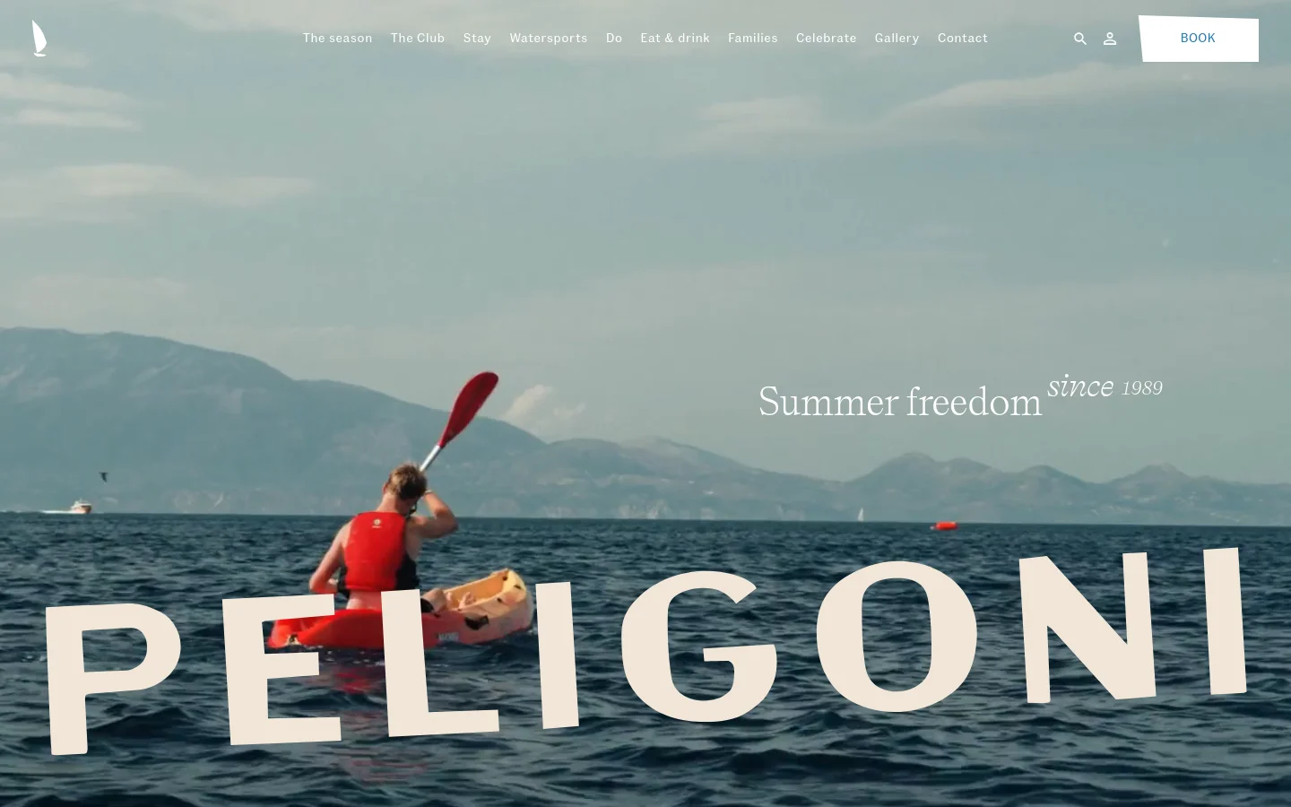 The desktop homepage features a large hero image of a person in a red kayak on blue water with mountains in the background. Large white text overlays the scene reading 'Summer freedom since 1989' and 'PELIGONI'. A top navigation bar includes links for The season, The Club, Stay, and more, alongside a prominent 'BOOK' button.