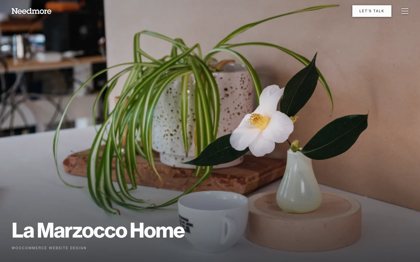 A portfolio page for La Marzocco Home featuring a large lifestyle hero image of a white flower and a spider plant in a speckled pot next to a coffee cup. The layout includes a dark overlay at the bottom with the headline 'La Marzocco Home' and a 'WooCommerce website design' subheadline. A navigation bar at the top contains the Needmore logo, a 'LET'S TALK' call to action button, and a hamburger menu icon.