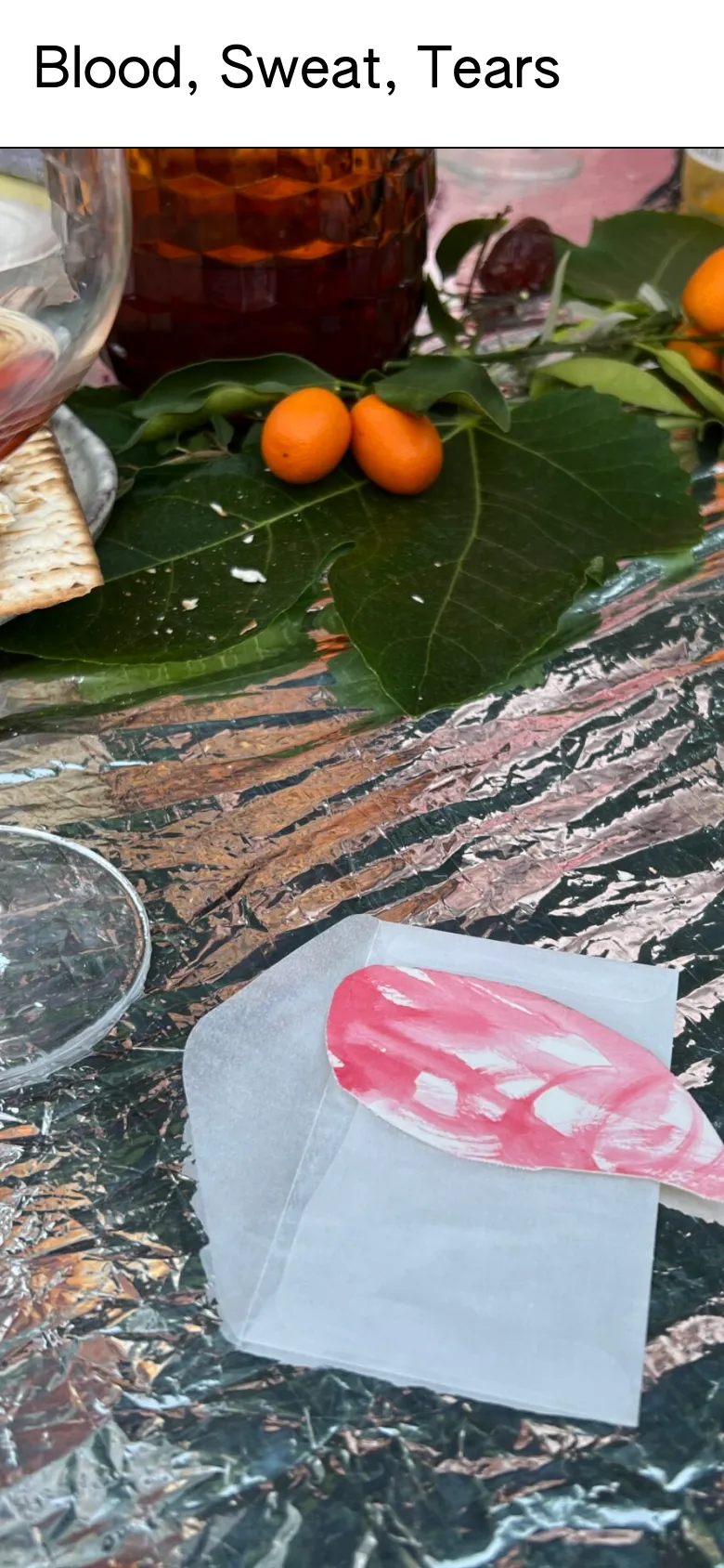 The mobile version displays a vertically oriented view of the Seder table, focusing closely on the citrus, green leaves, and the pink tear-shaped note. The headline 'Blood, Sweat, Tears' is prominently centered above the image, and the layout is simplified to prioritize the large-scale photography.