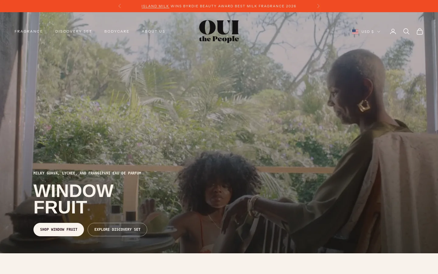 Desktop homepage featuring a large hero image of two women in a lush, tropical outdoor setting. The headline 'WINDOW FRUIT' is prominently displayed in white over the image, accompanied by buttons to 'SHOP WINDOW FRUIT' and 'EXPLORE DISCOVERY SET'. A navigation menu sits at the top with links for Fragrance, Discovery Set, Bodycare, and About Us, alongside a brand logo and utility icons.