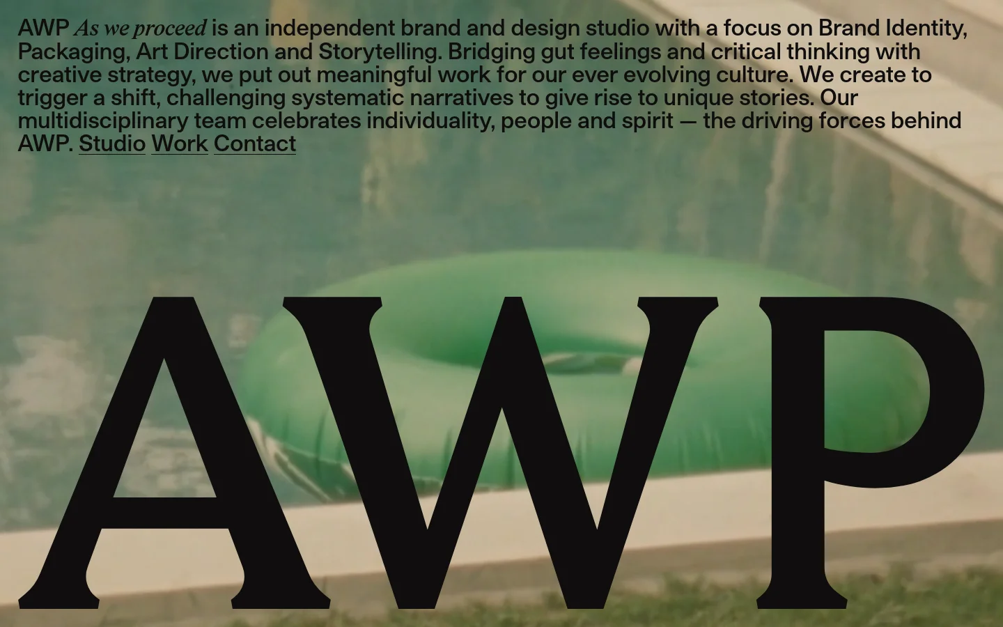 The desktop homepage features a large hero section with the bold black text 'AWP' overlaid on a blurred background image of a green inflatable ring. Above the large text, a paragraph describes the studio's focus on brand identity and storytelling, followed by navigation links for Studio, Work, and Contact. Below the hero, a grid of large project images showcases various works like ERE Studios and Vampons.
