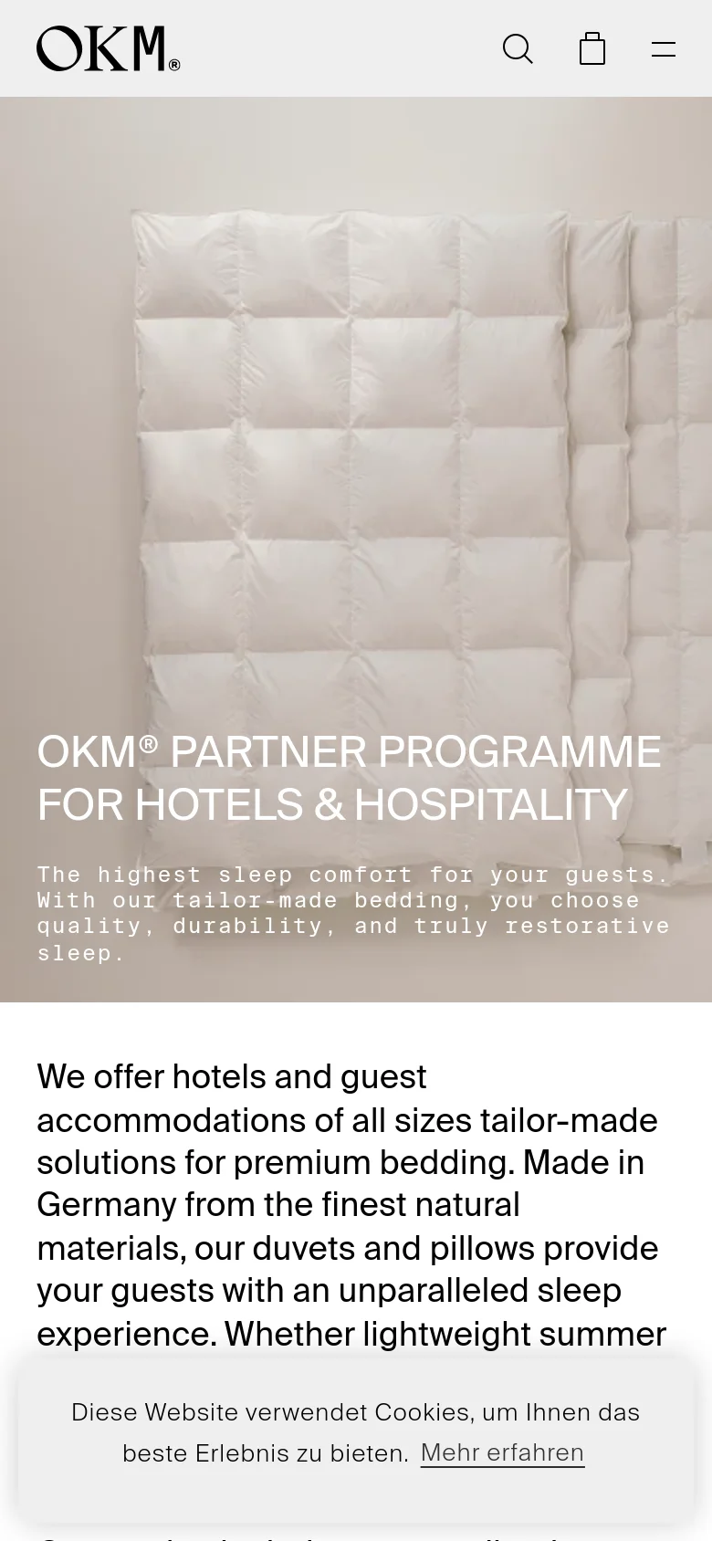 The mobile version presents a vertically stacked layout, starting with the OKM logo, a search icon, a shopping bag icon, and a hamburger menu icon. The hero image of white duvets is scaled to fit the narrow screen, with the main headline and subtext centered over the image. A cookie consent banner appears at the bottom of the screen over the content.