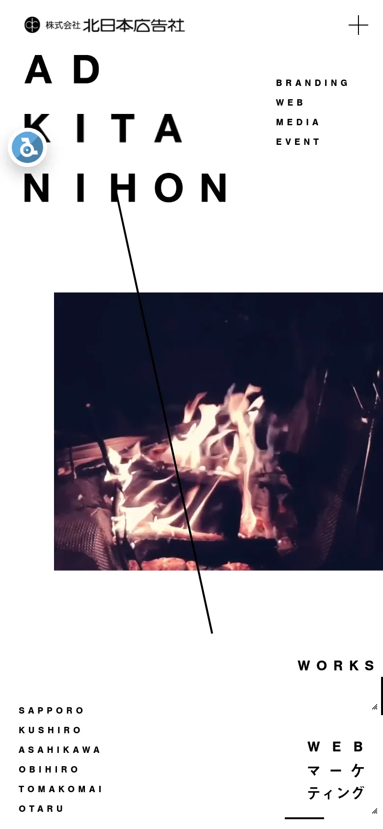 The mobile version presents a vertically stacked layout with a prominent hamburger menu icon in the top right. The large 'AD KITANIHON' branding dominates the top section, followed by service categories like 'Branding' and 'Web' and a full-width hero image of a campfire. The branch locations are listed vertically towards the bottom of the screen.