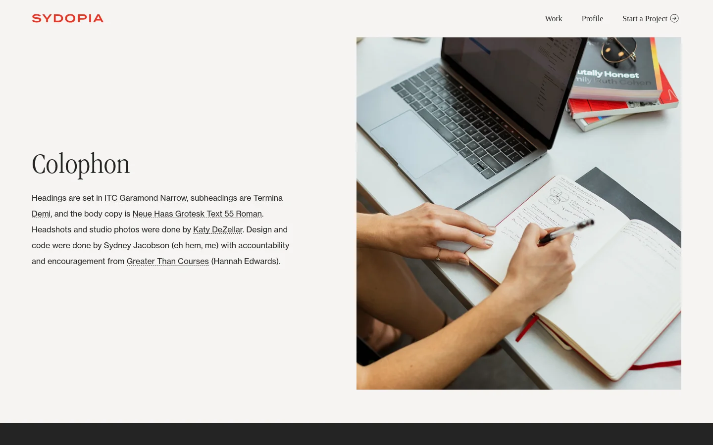 The Colophon page features a minimalist layout with a white background and red Sydopia logo in the top left. On the left, a large serif heading 'Colophon' sits above descriptive text about typography and credits, while the right side is occupied by a large vertical photograph of a person writing in a notebook next to a laptop. The desktop navigation includes links for Work, Profile, and Start a Project.