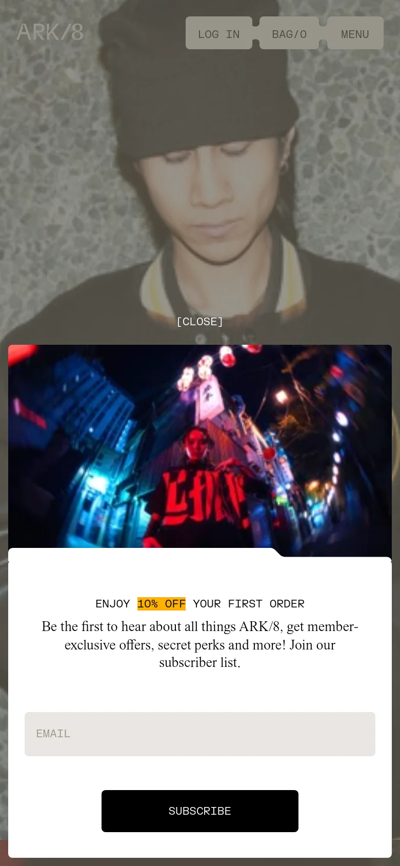 The mobile version displays a vertically oriented pop-up for a 10% discount, featuring a vibrant, neon-lit street scene image. The navigation is condensed into a 'MENU' button alongside 'LOG IN' and 'BAG/0' links at the top, and the text is scaled for easier reading on a smaller screen.