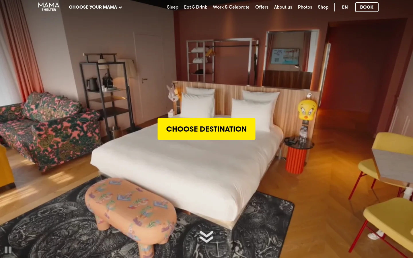 The desktop homepage features a large hero image of a stylish, colorful hotel room with a white bed and patterned furniture. A prominent yellow 'CHOOSE DESTINATION' button is centered over the image, and the navigation bar at the top includes links for Sleep, Eat & Drink, and Work & Celebrate, alongside a 'BOOK' button. The color palette is warm with wood tones, pinks, and bright yellow accents.