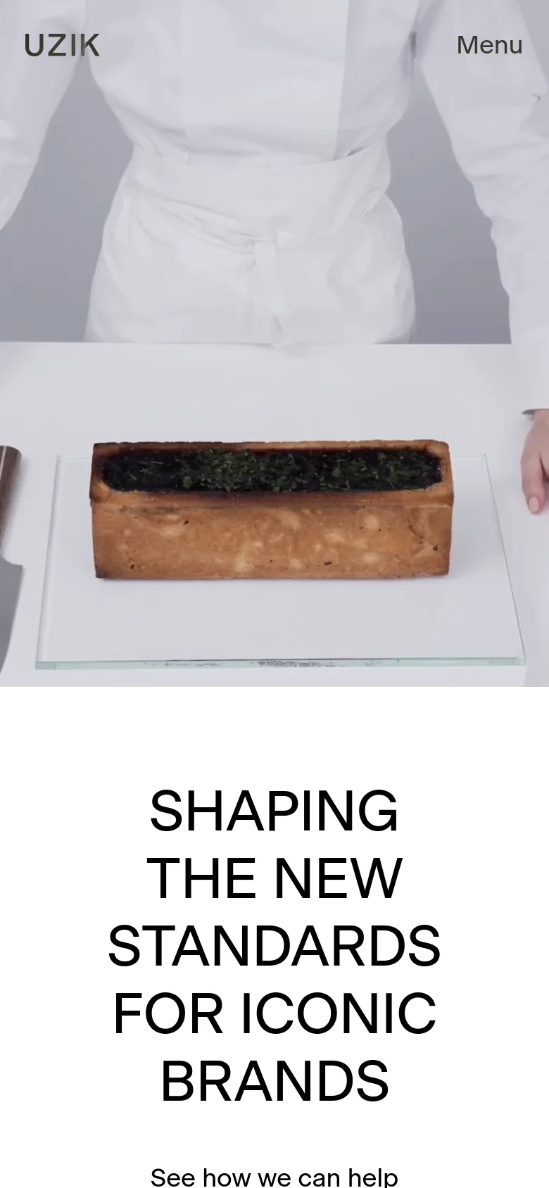 The mobile version maintains the minimalist aesthetic with the 'UZIK' logo and 'Menu' at the top. The layout is vertically oriented, focusing on the large hero image of a culinary presentation followed by the centered, bold headline 'SHAPING THE NEW STANDARDS FOR ICONIC BRANDS' and a call to action link.