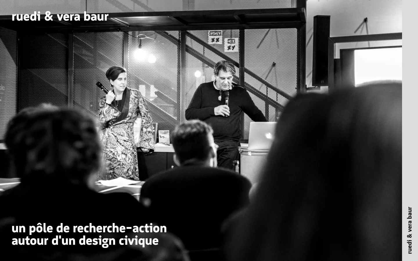 A minimalist desktop homepage featuring a large black and white hero photograph of two people presenting to an audience in an industrial setting. The text 'ruedi & vera baur' is in the top left, and the headline 'un pôle de recherche-action autour d'un design civique' appears in the bottom left over the image. The layout is clean with high contrast and a monochromatic color scheme.