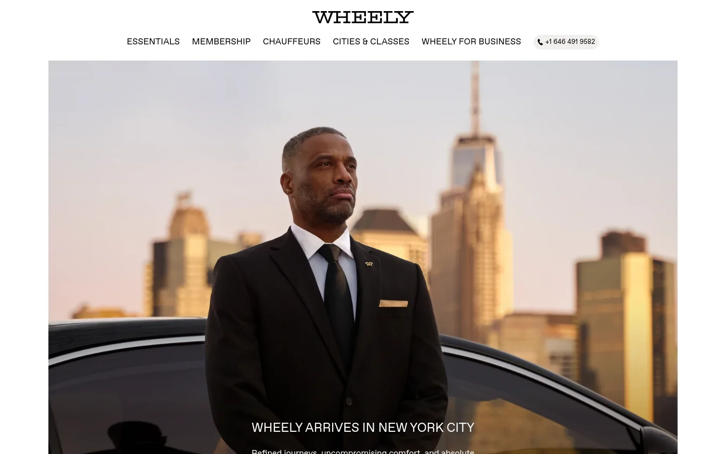 The Wheely homepage features a hero image of a chauffeur in a black suit standing before a city skyline at sunset. A navigation bar at the top includes links for Essentials, Membership, Chauffeurs, Cities & Classes, and Wheely for Business, alongside a phone number button. The main headline reads 'WHEELY ARRIVES IN NEW YORK CITY' with a 'DISCOVER MORE' call to action.