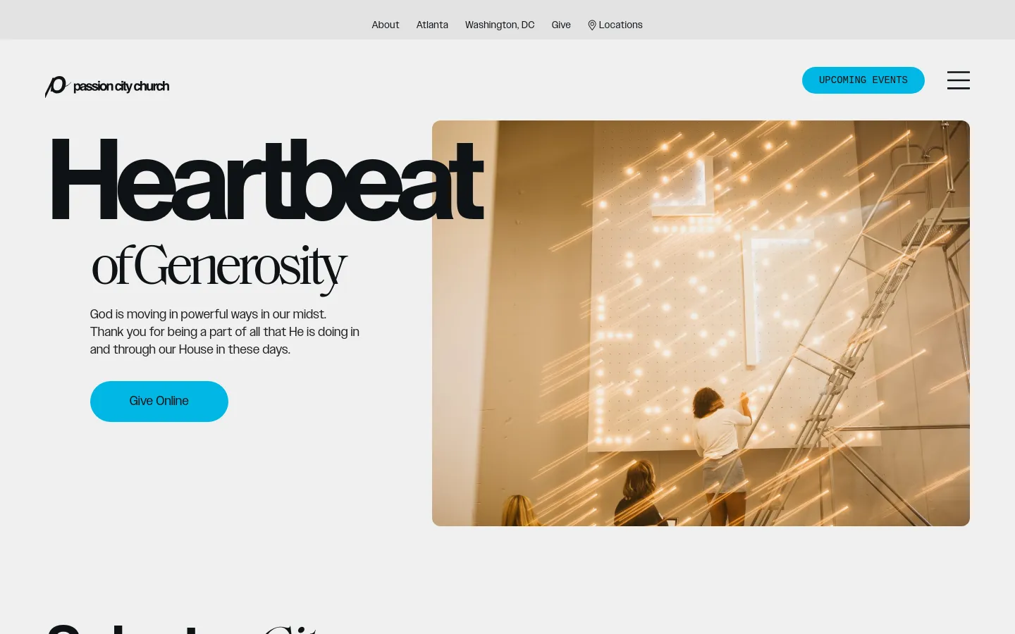 The desktop page features a large hero section with the headline 'Heartbeat of Generosity' in bold black text next to a warm-toned photograph of people working on a light installation. A bright blue 'Give Online' button is positioned below a short paragraph of text, set against a clean white background with a navigation menu at the top.