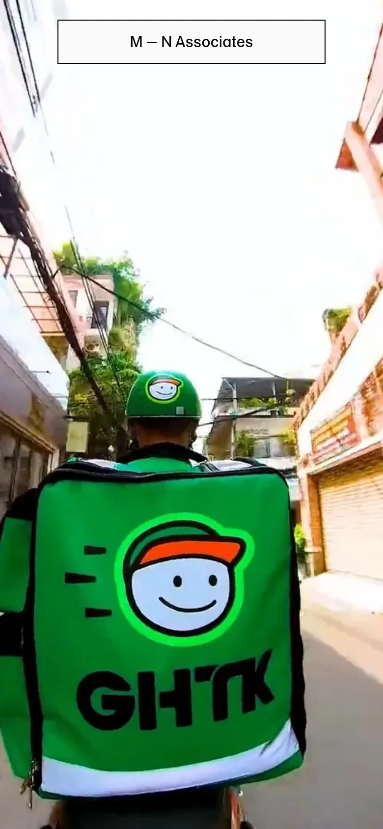 The mobile version displays a vertical layout focusing on a single large project feature. It shows a close-up, high-angle shot of a delivery person wearing a green helmet and a large green 'GHTK' backpack, riding through a narrow urban street. The 'M — N Associates' logo is centered at the top in a white rectangular box.