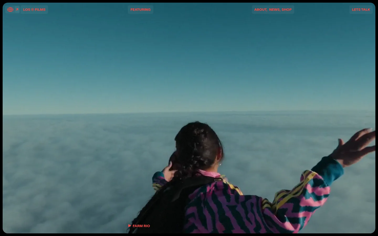 Los Films homepage featuring a full-bleed cinematic video background of a person in a patterned jacket looking over clouds. The minimalist navigation includes links for Featuring, About, News, and Shop, set against a teal and soft white color palette with coral-toned typography.