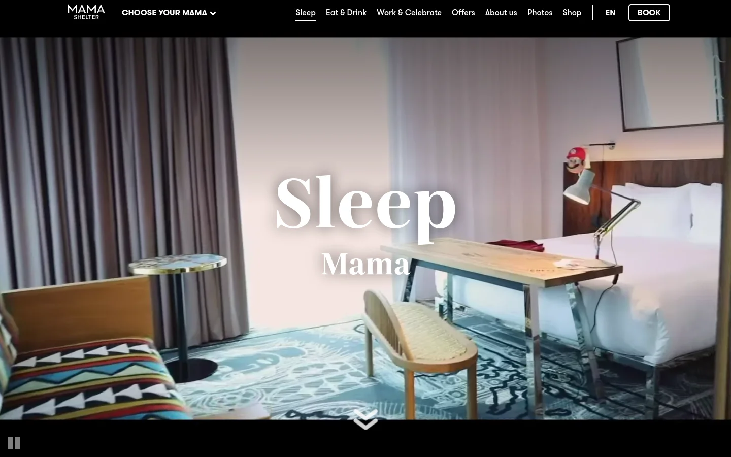 The desktop page features a large hero image of a stylishly designed bedroom with a desk and bed, overlaid with the large white text 'Sleep Mama'. A top navigation bar includes the Mama Shelter logo, menu links like 'Sleep' and 'Eat & Drink', and a prominent 'BOOK' button. The layout is clean with a dark header and a large, immersive visual focus.