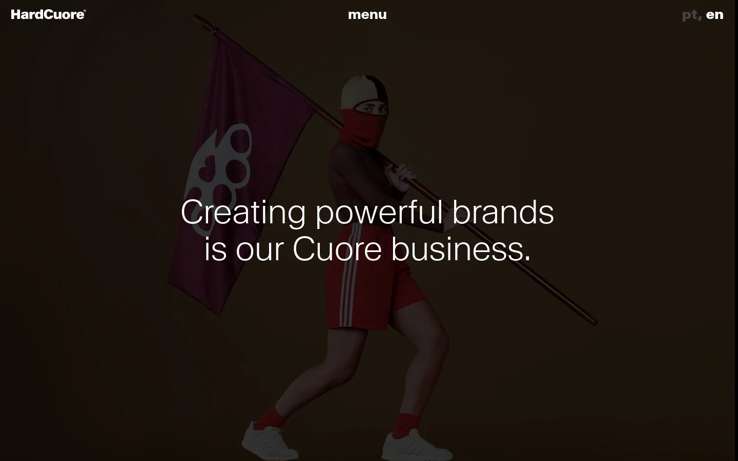 The desktop About page features a dark brown background with a large hero image of a person in red athletic wear holding a flag. A large white headline reads, 'Creating powerful brands is our Cuore business.' The navigation includes the HardCuore logo, a menu button, and language toggles.