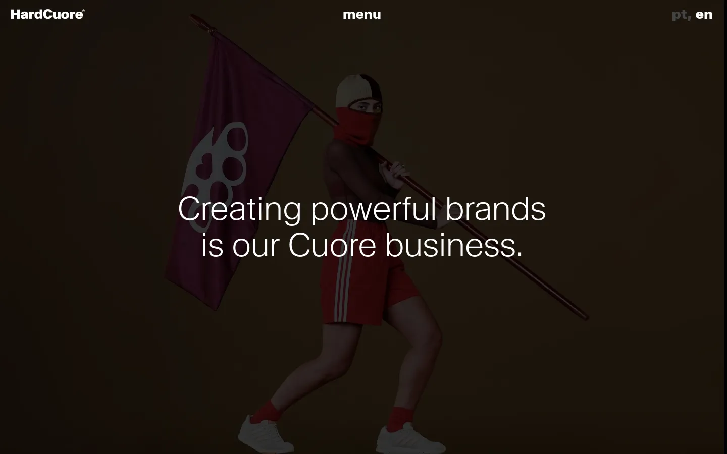 The desktop About page features a dark brown background with a large hero image of a person in red athletic wear holding a flag. A large white headline reads, 'Creating powerful brands is our Cuore business.' The navigation includes the HardCuore logo, a menu button, and language toggles.