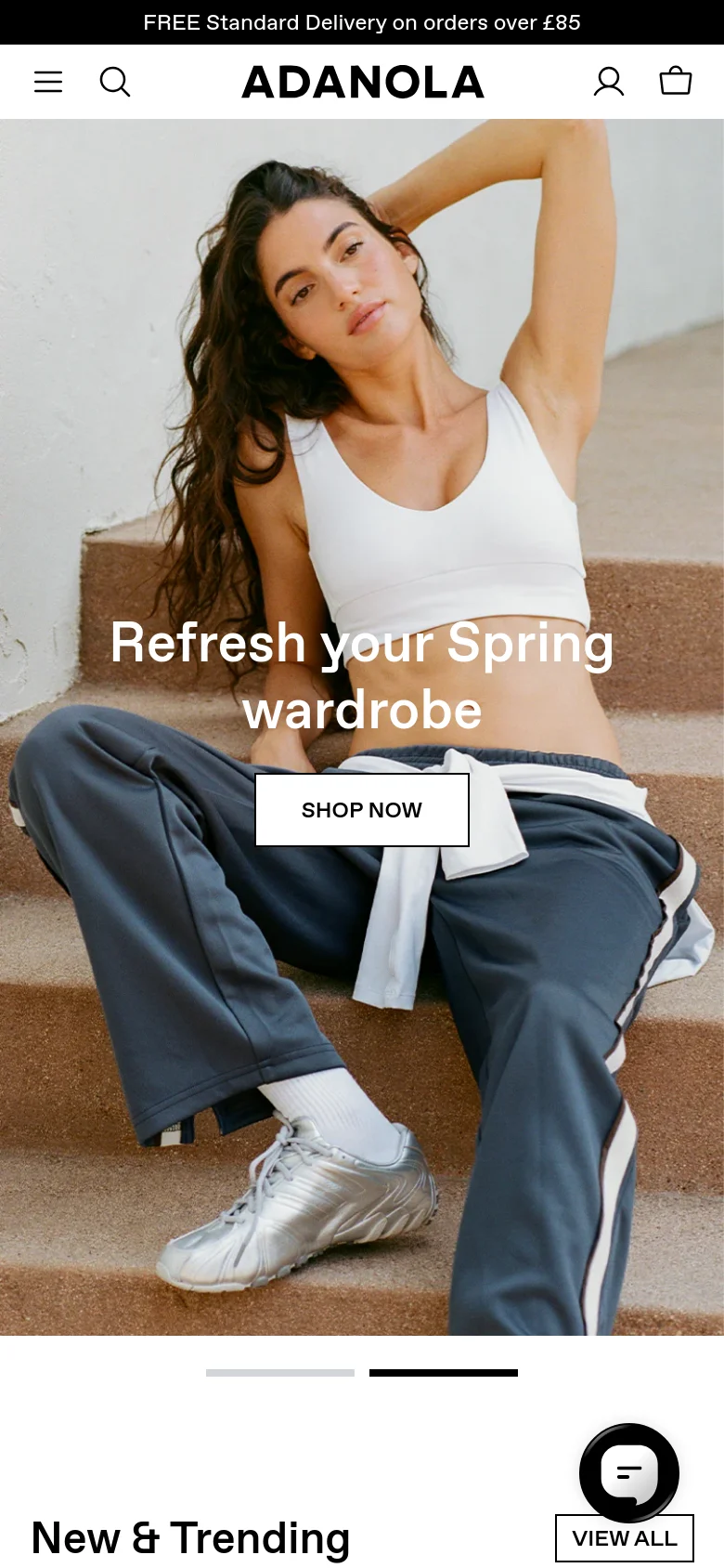 The mobile version uses a vertical, single-image hero shot of a woman in a white sports bra and grey joggers, with the text 'Refresh your Spring wardrobe' and a 'SHOP NOW' button centered over the image. The navigation is condensed into a hamburger menu and search icon at the top, and the 'New & Trending' section follows below.