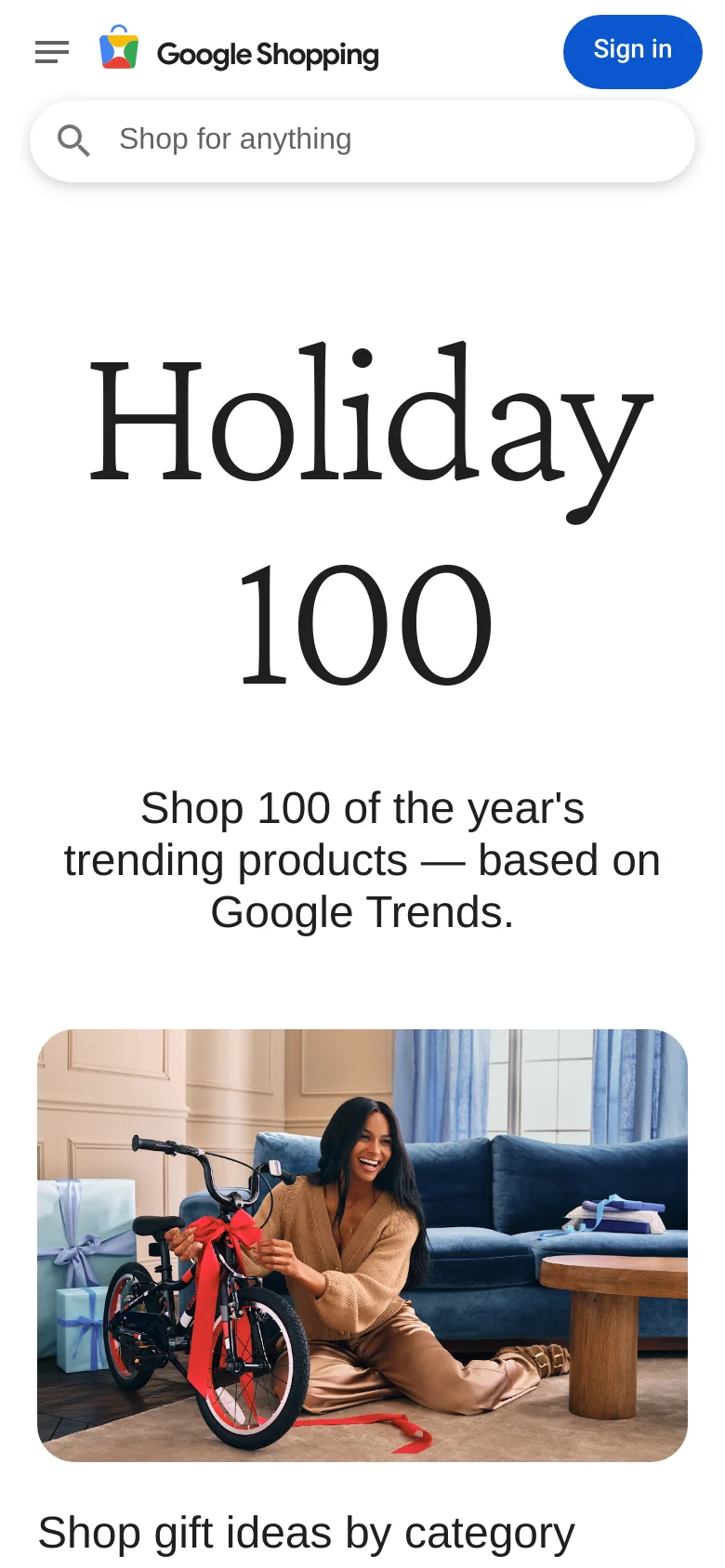 The mobile version presents a vertically stacked layout with the Holiday 100 headline and subtext centered above the hero image. The header is condensed, featuring a hamburger menu, the Google Shopping logo, and a Sign in button, with the search bar positioned prominently below them. The overall color scheme remains white and blue, optimized for a narrow screen.