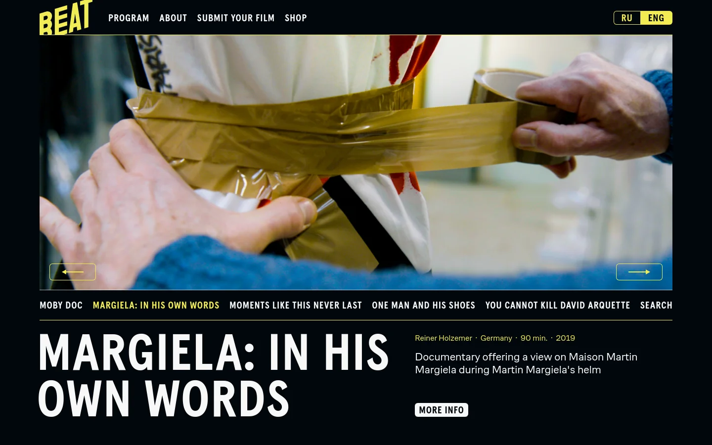 The Beat Film Festival homepage features a dark theme with a large cinematic hero image of hands applying tape to a white garment. A navigation bar at the top includes links for Program, About, Submit Your Film, and Shop, alongside language toggles. Below the hero section, a film showcase displays titles like 'Margiela: In His Own Words' with large white typography against a black background and a 'More Info' button.